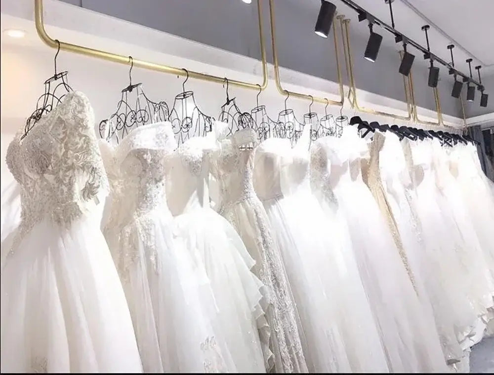 Collection of white short wedding dress gowns with lace and tulle details hanging on gold rack in bridal shop