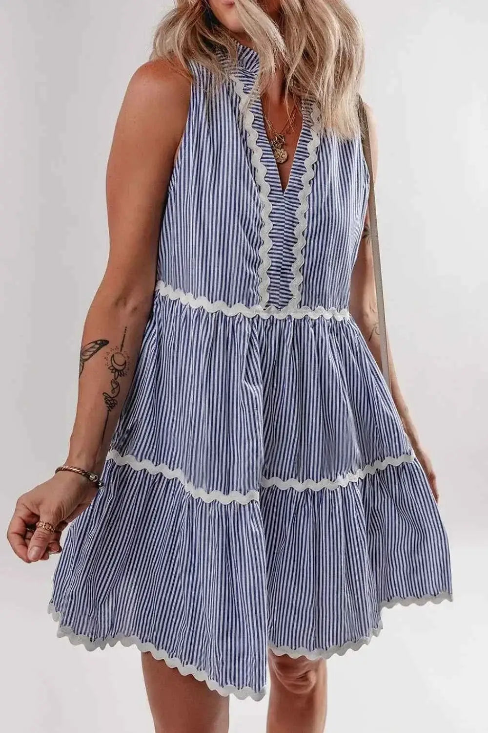 Sleeveless mini dress in blue and white vertical stripes with tiered skirt, notched neckline, and white ric rac trim featuring frills, showcasing the Stripe Sleeveless Notched Ric Rac Mini Dress design