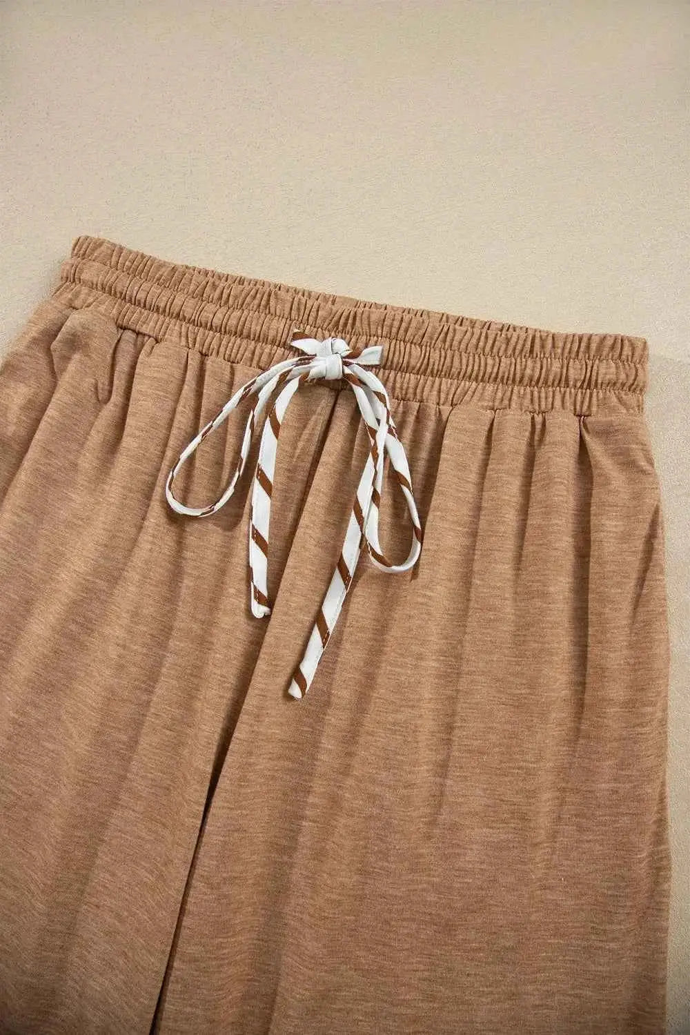 Beige drawstring pants with white and brown striped tie detail, soft cotton blend fabric with moderate stretch