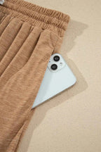 Drawstring pants in light brown cotton blend fabric with elastic waistband and side pocket holding a white smartphone