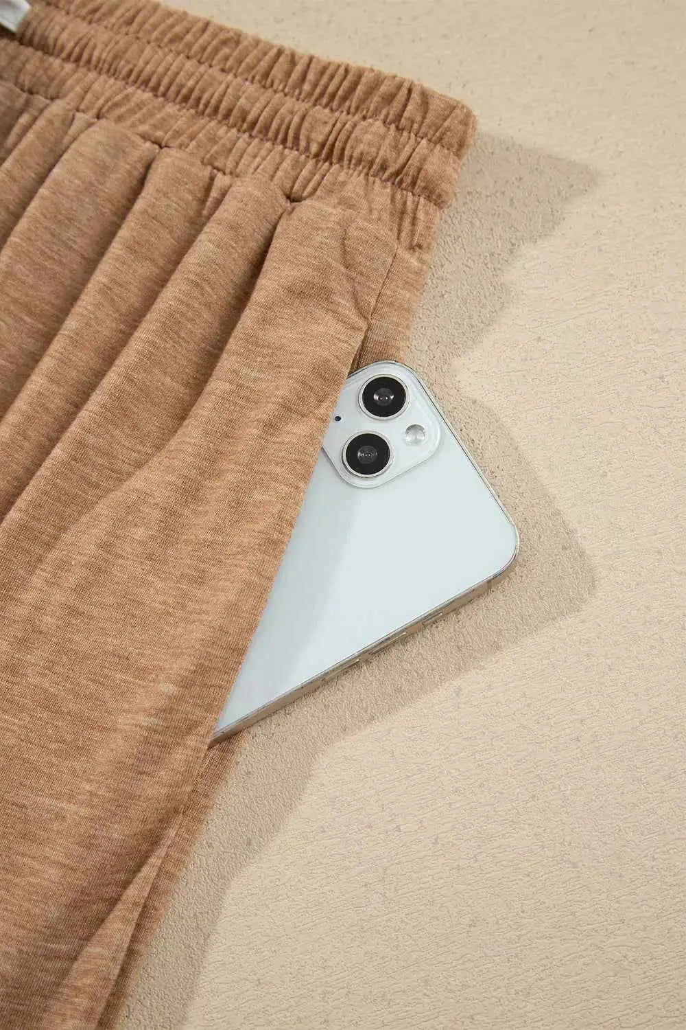 Drawstring pants in light brown cotton blend fabric with elastic waistband and side pocket holding a white smartphone