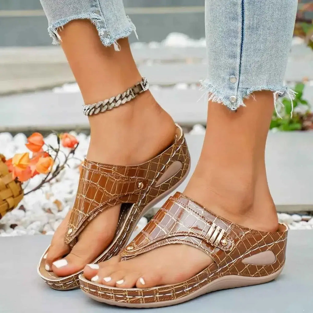 Toe Post Wedge Sandals in brown PU leather with crocodile pattern and mid-height rubber wedge heels on feet with anklet