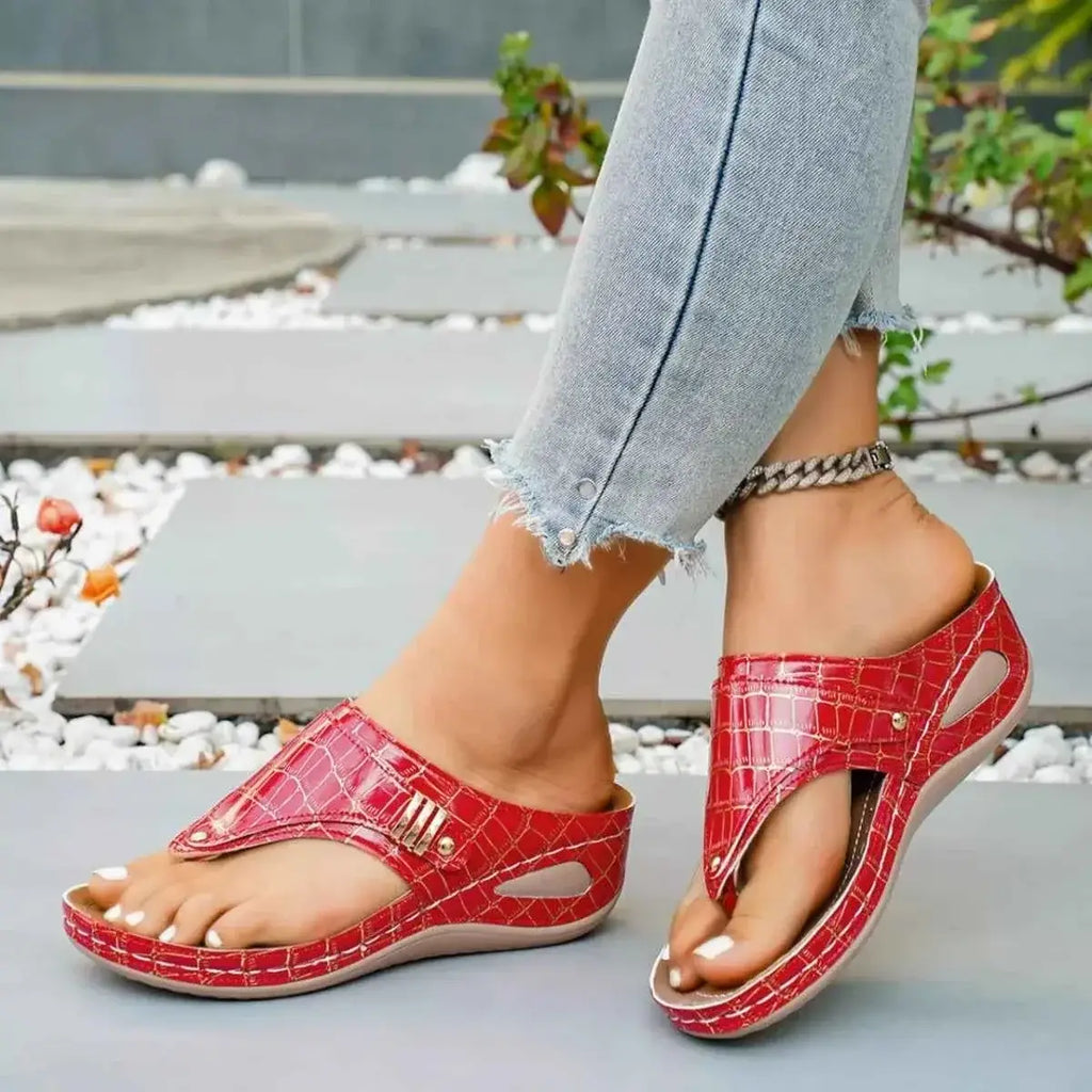 Red croc pattern Toe Post Wedge Sandals in PU leather with gray rubber wedge soles worn with ankle chain and light denim jeans